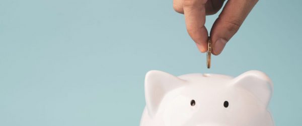 Hand putting coin to white piggy bank saving on blue background and copy space , Money saving for future investment and retirement concept.