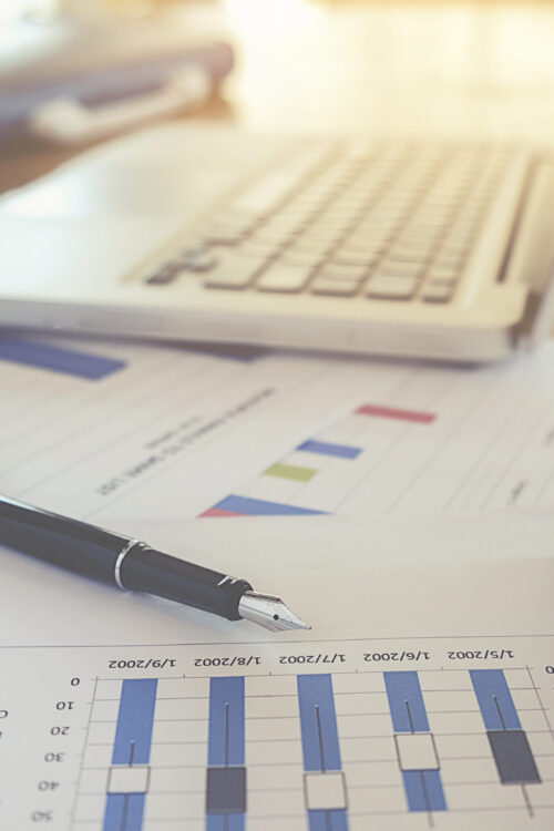 Business concept with copy space. Office desk table with pen focus and analysis chart, computer, notebook, cup of coffee on desk.Vintage tone Retro filter effect.Selective focus.